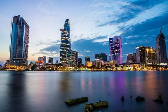 Ảnh thành phố với hệ thống tòa nhà cao tầng rực rỡ ánh sáng phản chiếu trên mặt nước vào buổi tối.