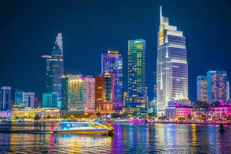 Ảnh thành phố ban đêm với tòa nhà cao tầng, ánh đèn neon và con thuyền trên sông.